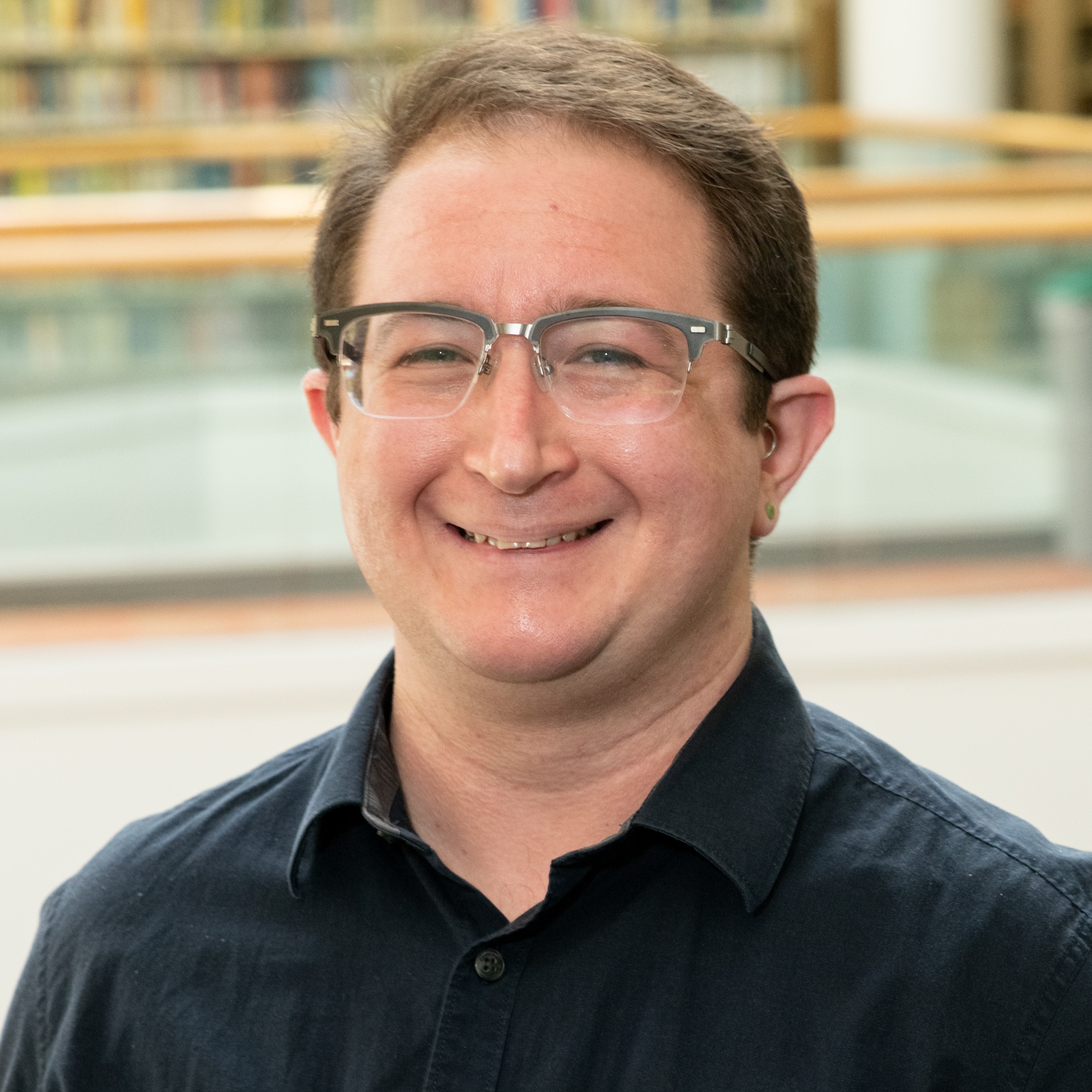 A headshot of Simon Ragovin smiling in the Hagerty Library wearing a black button down shirt.